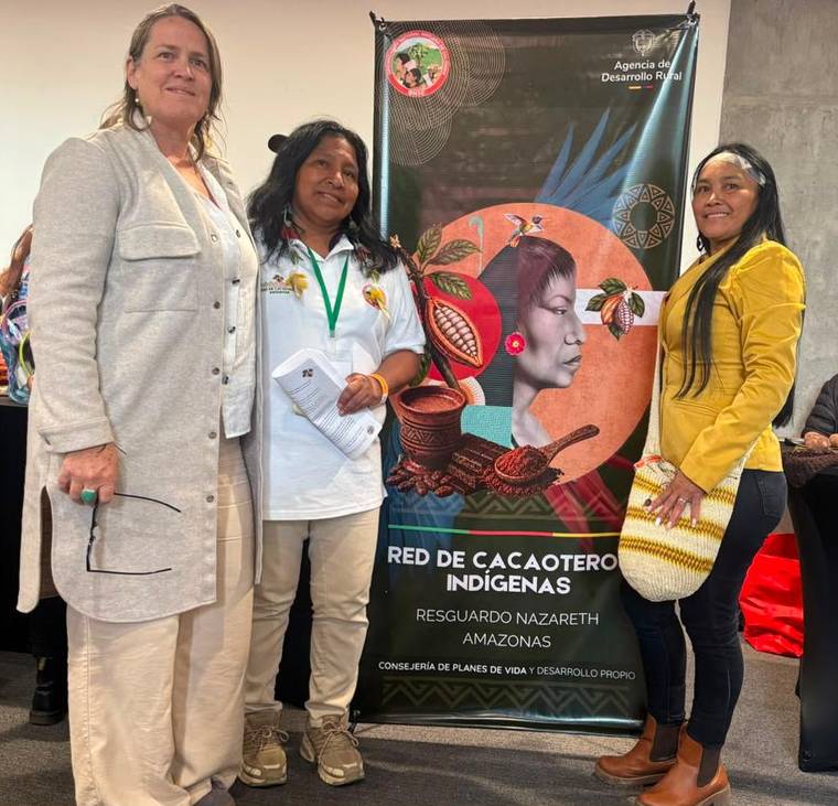Sheila Gruner y Clemencia Herrera, del IPTP, con Regina Dutcha de la OPIAC, ante el pendón de la Red de Cacaoteros Indígenas del Resguardo Nazareth, Amazonas.