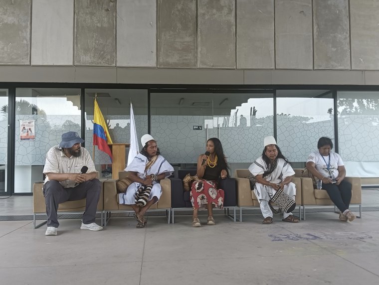 Cinco personas sentadas en un conversatorio sobre educación propia en la Universidad Nacional de Colombia, sede La Paz, Cesar, con estudiantes de Algoma University de Canadá entre el público.